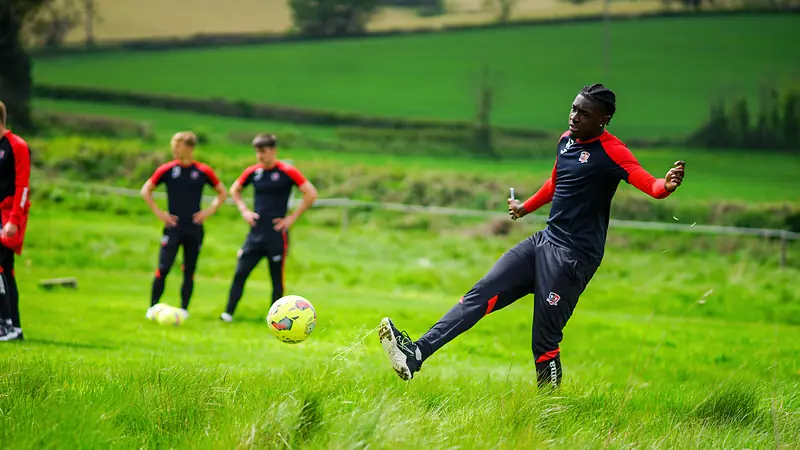 A player striking a football while teammates watch at Escot Park
